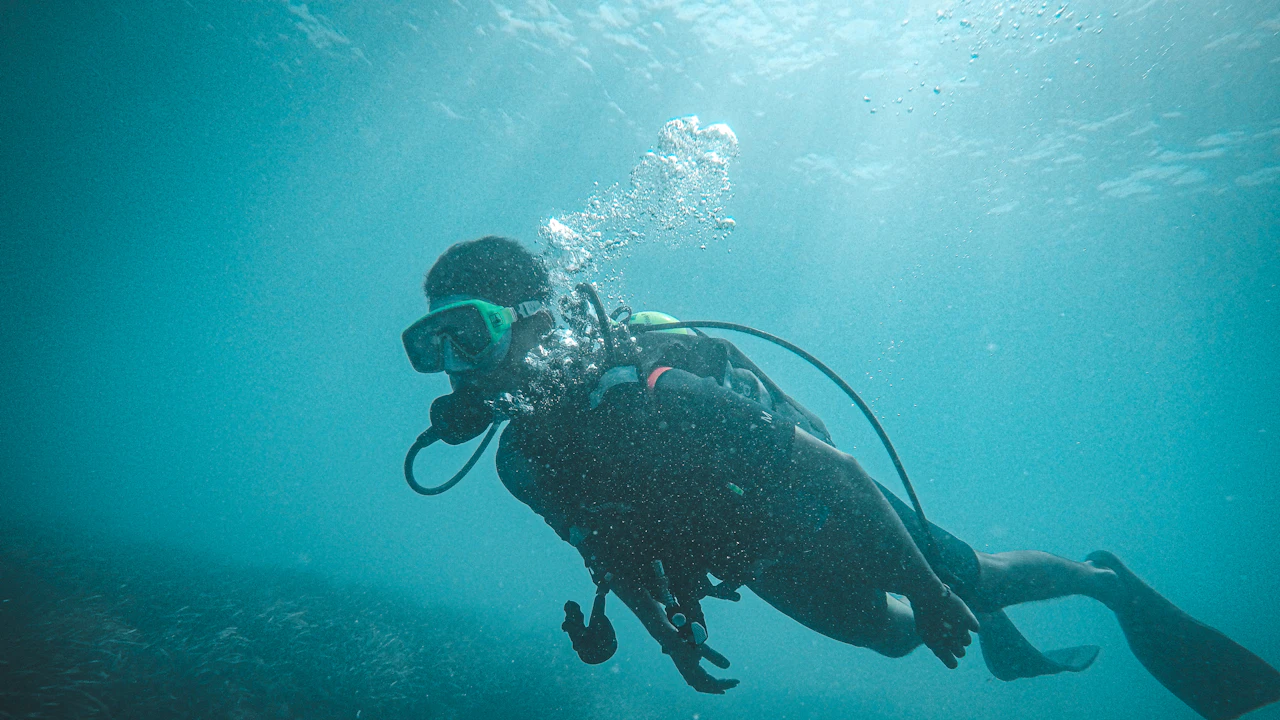 Scuba diver swimming through blue-green water with bubbles rising