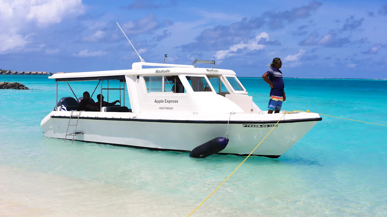 Small white boat moored in turquoise shallows with a crew member aboard