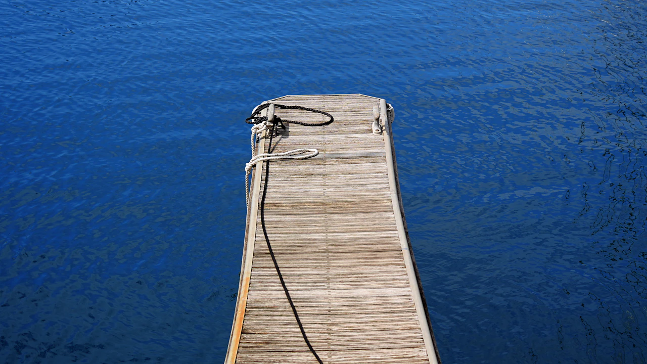 Wooden dock with a coiled rope over deep blue water