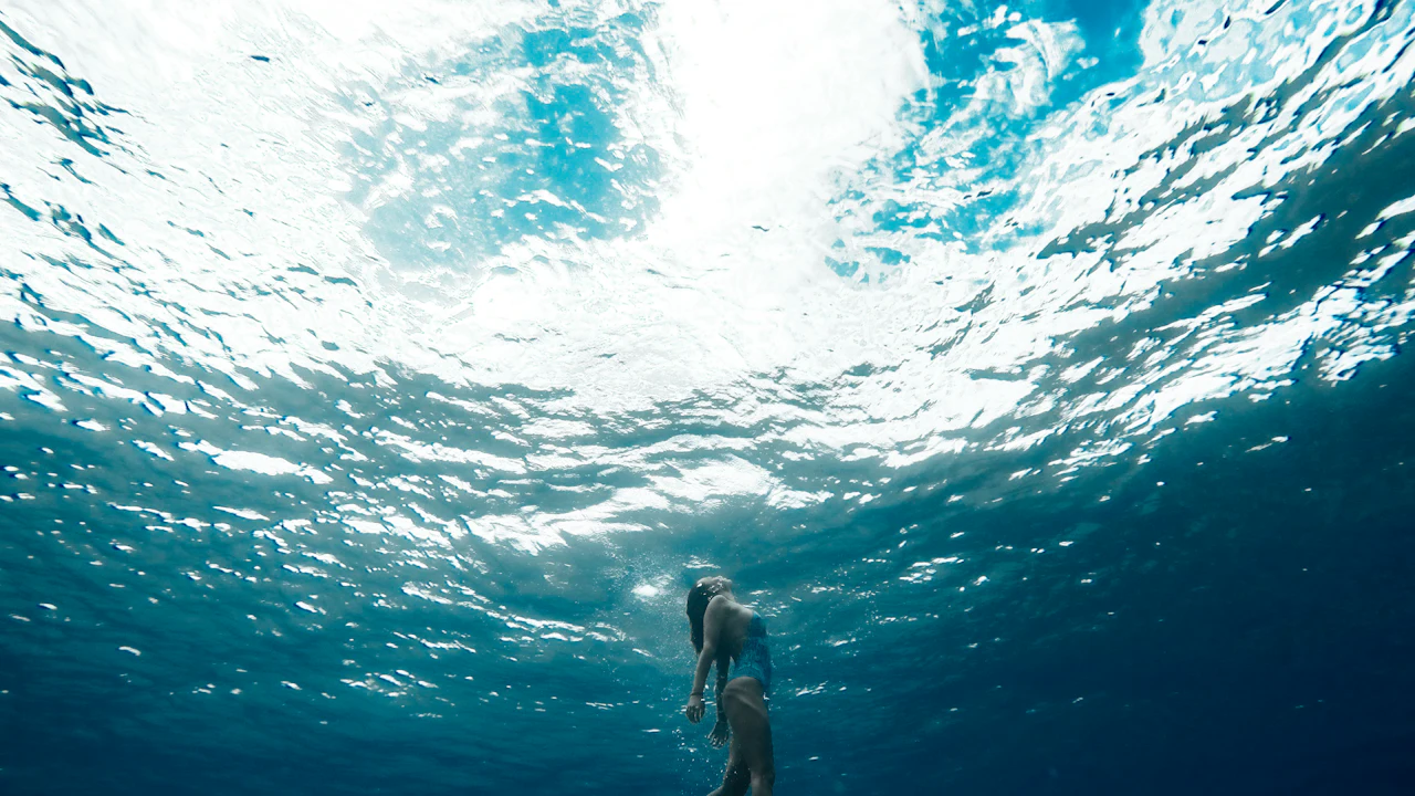 Swimmer seen from below the bright water surface