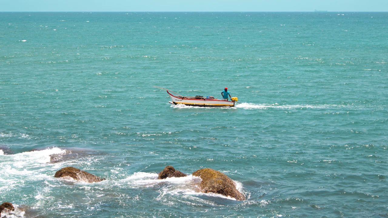Small fishing boat crossing turquoise water past rocks