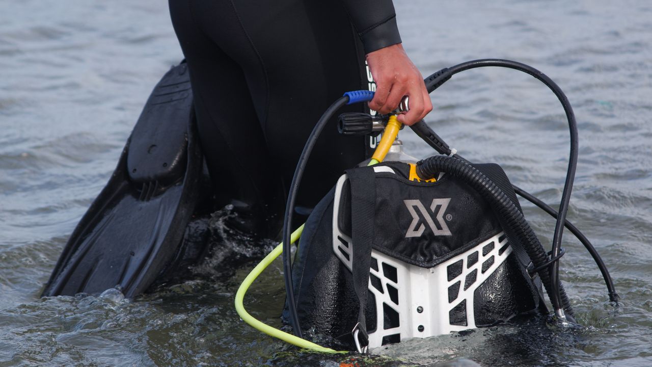 Diver carrying a BCD with regulator hoses into the water
