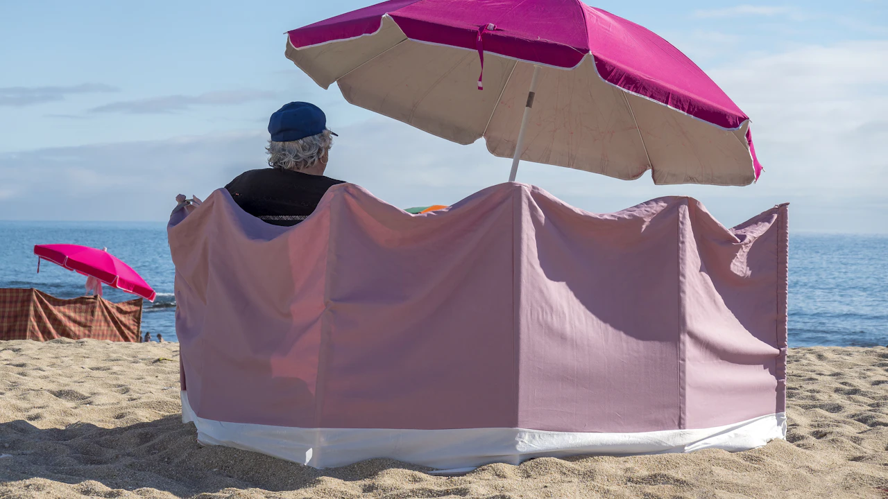 Person sitting under a pink beach umbrella behind a windbreak