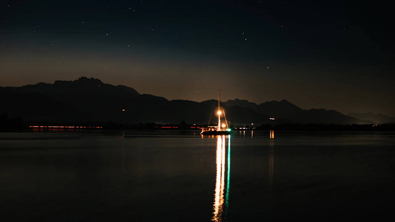 Boat with deck lights on floating on calm dark water at night
