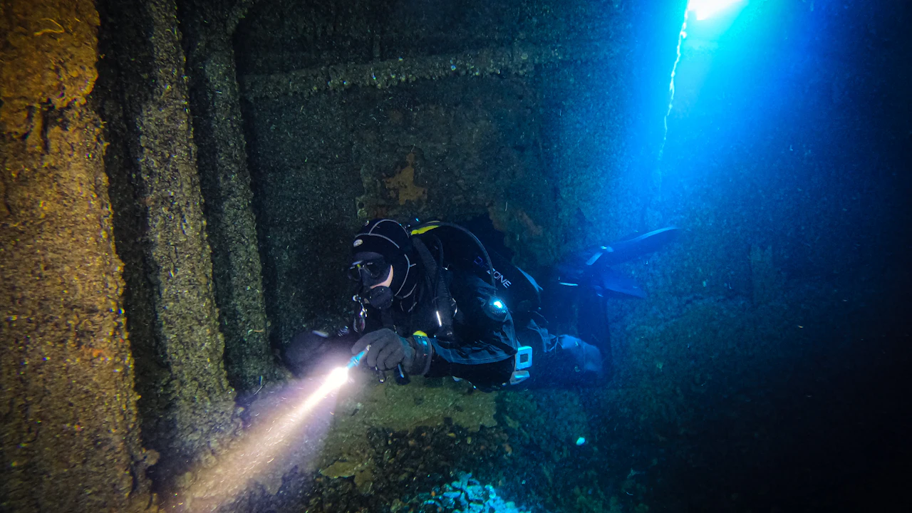Scuba diver holding a dive torch in dark water during a night dive