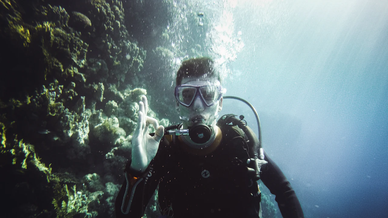 Scuba diver giving the OK sign beside a rock wall