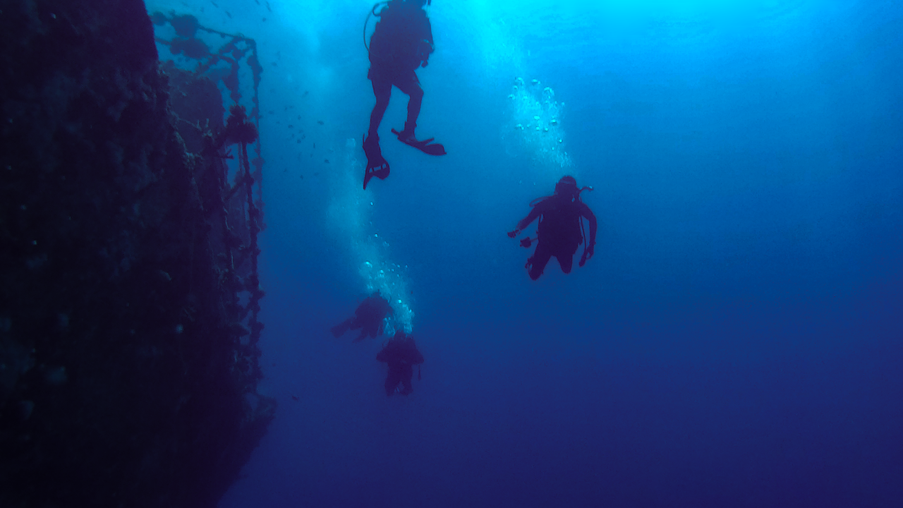 Two scuba divers descending beside a steep rock wall into deep blue water