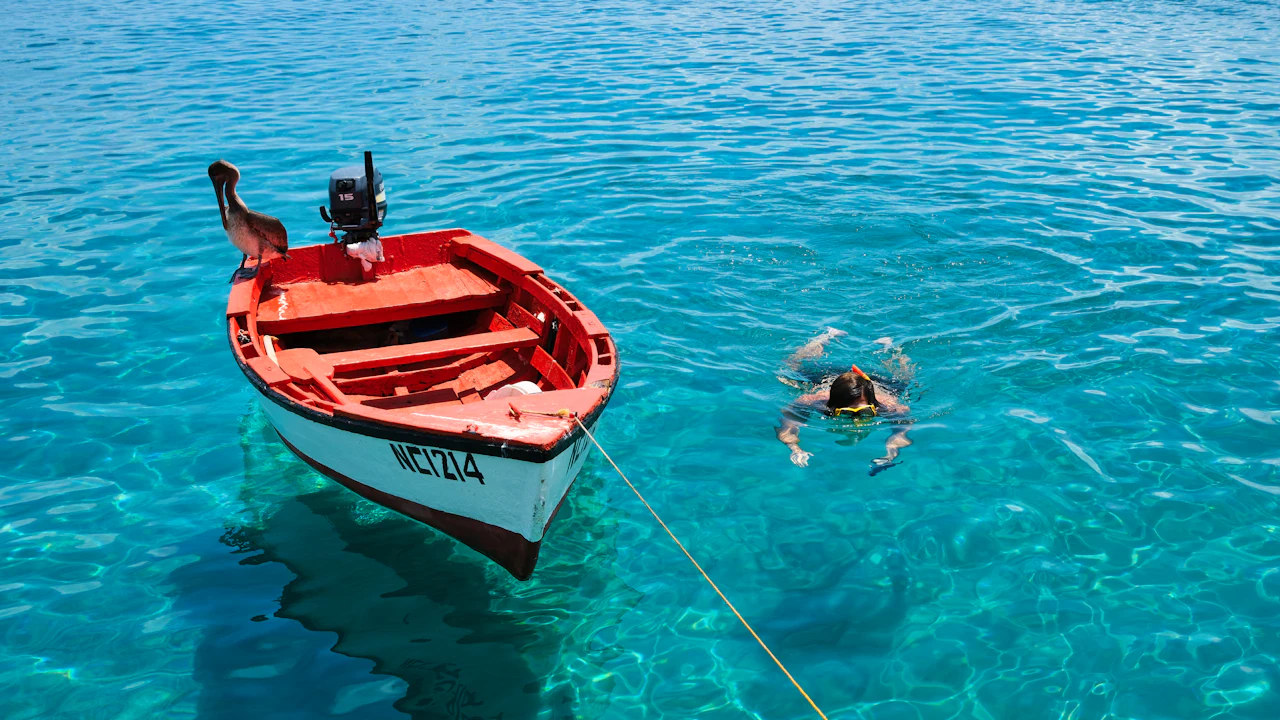 Small red boat moored over clear turquoise water with a snorkeler nearby