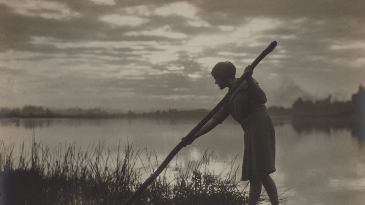 Person poling a boat across calm water in a vintage photo