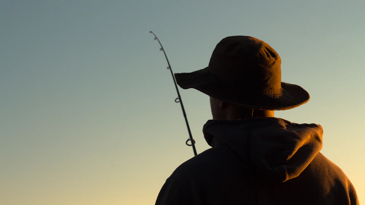 Angler in a wide-brimmed hat holding a fishing rod at sunset