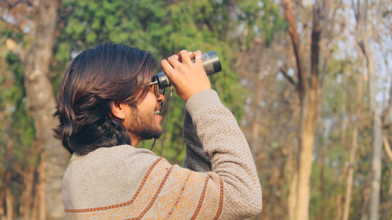 Man looking through binoculars in a forest