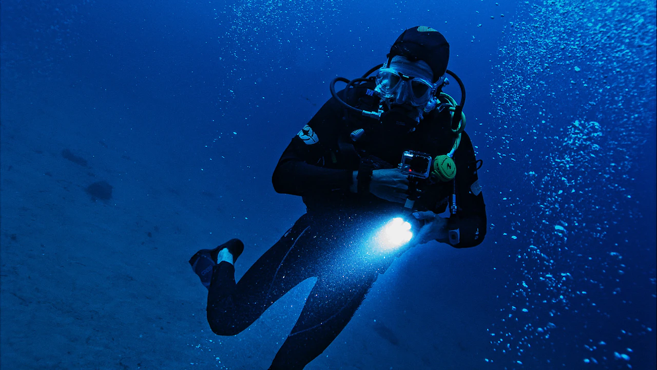 Diver with a dive light hovering in deep blue water