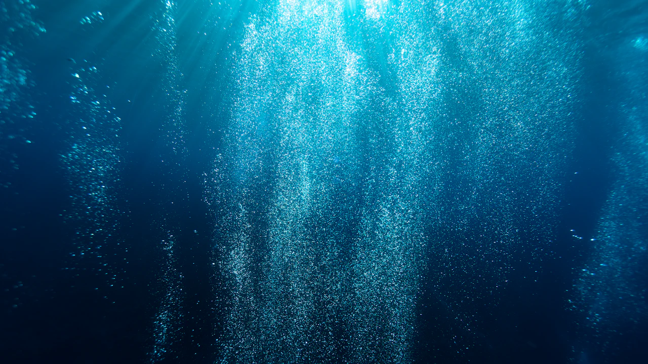 Diver breathing out a steady stream of bubbles in clear blue water