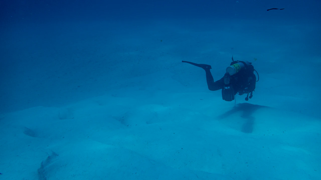 Diver hovering just above a sandy bottom in clear blue water