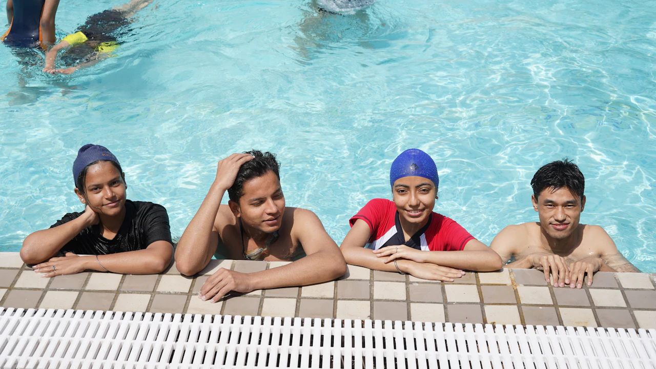 Four young swimmers in caps resting at the edge of a pool