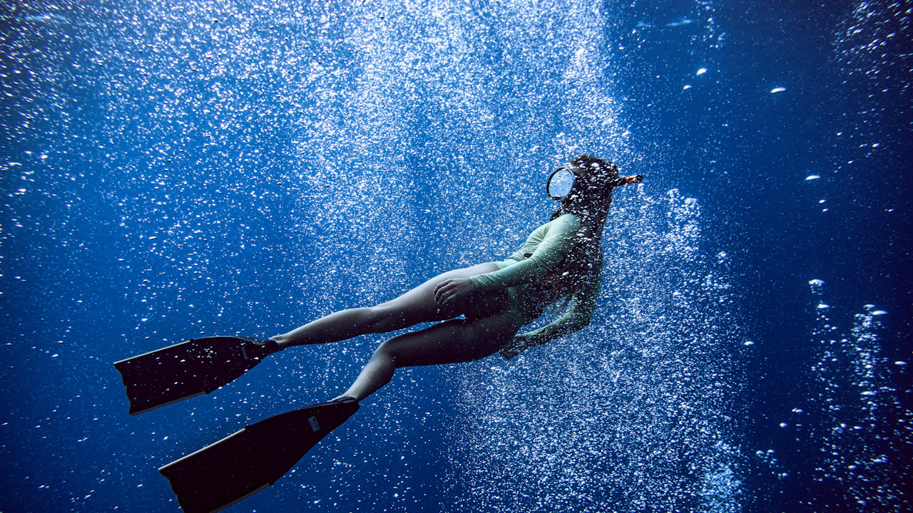 Free diver gliding up through bubbles in blue water