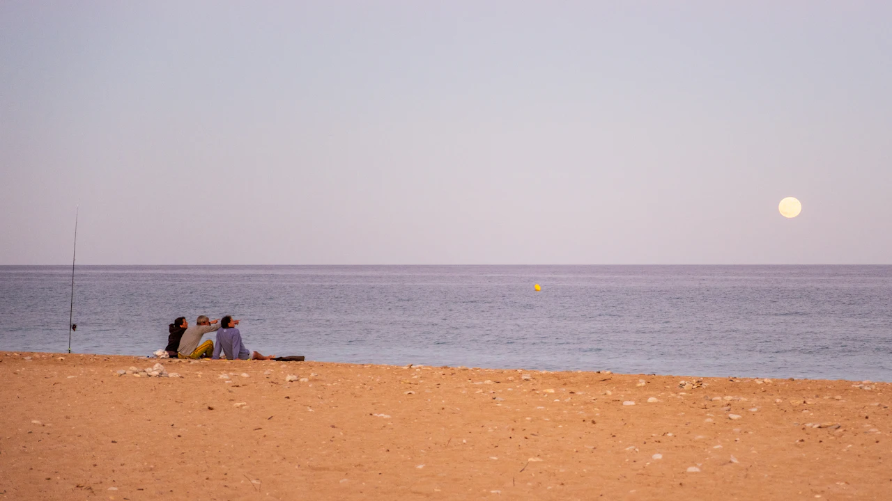 Full moon over a calm sea with people on the beach