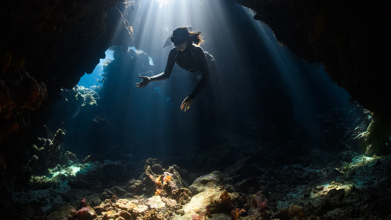 Diver swimming through a sunlit underwater cavern