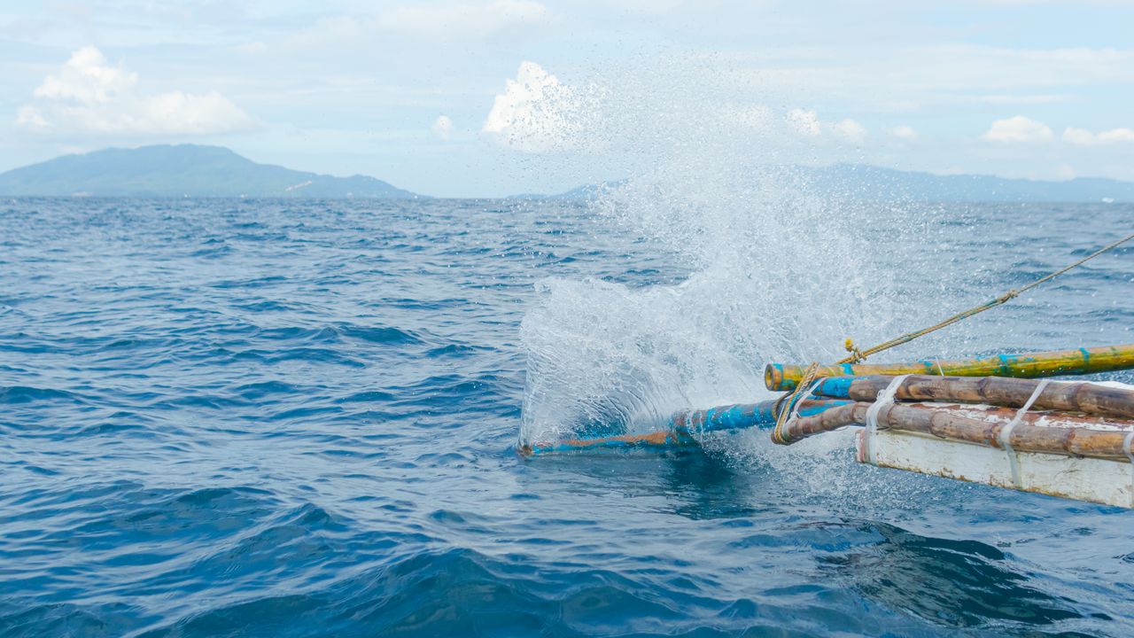 Outrigger fishing boat cruising across open sea