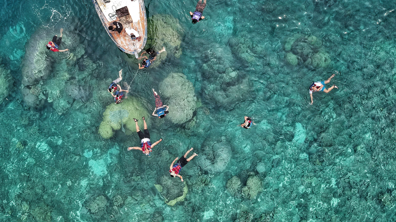 Aerial view of snorkelers swimming over coral heads beside an anchored boat