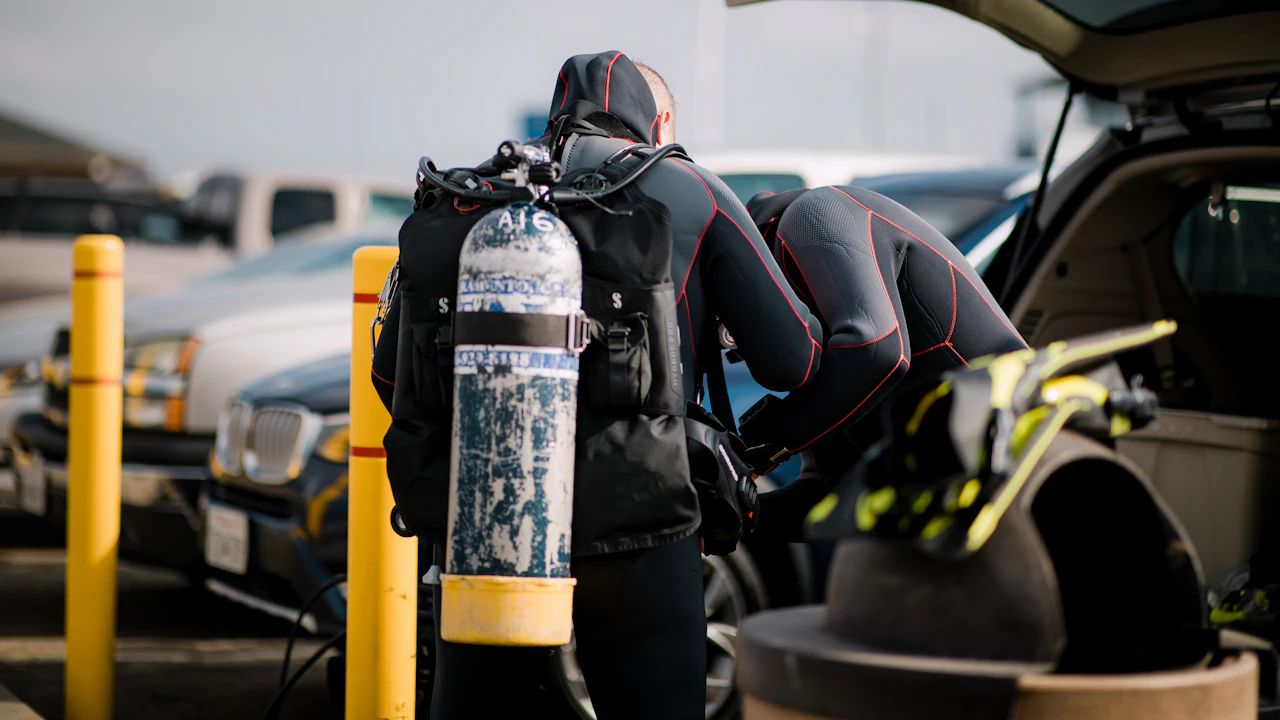 Divers in wetsuits putting on tanks beside a car