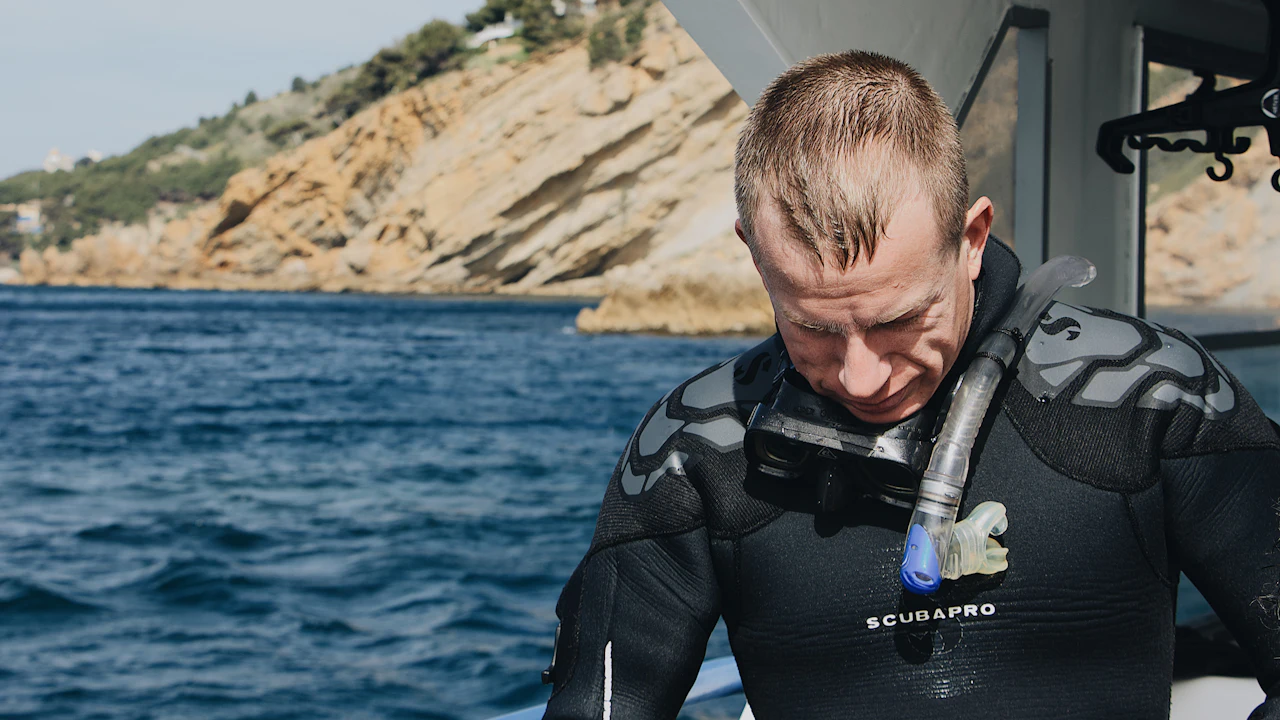 Diver in a wetsuit looking down at his gear on a boat