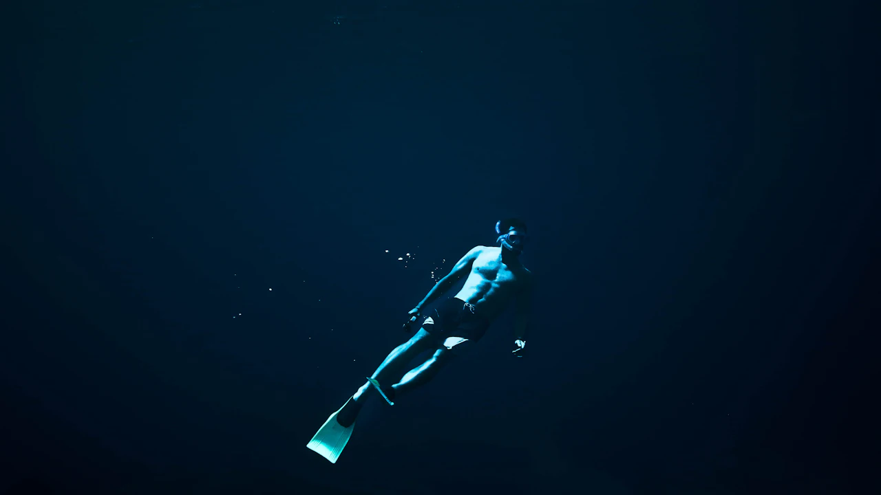 Free diver swimming up through dark blue water