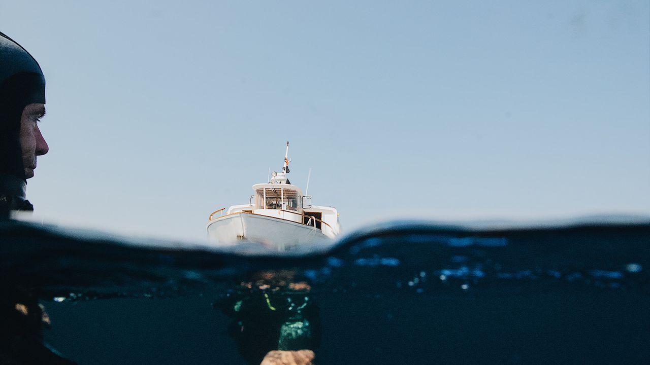 Diver in a hood at the surface looking toward a boat