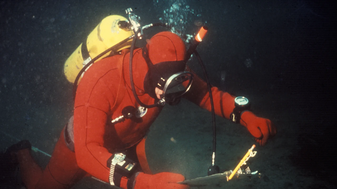 Diver in a red drysuit working underwater with a light