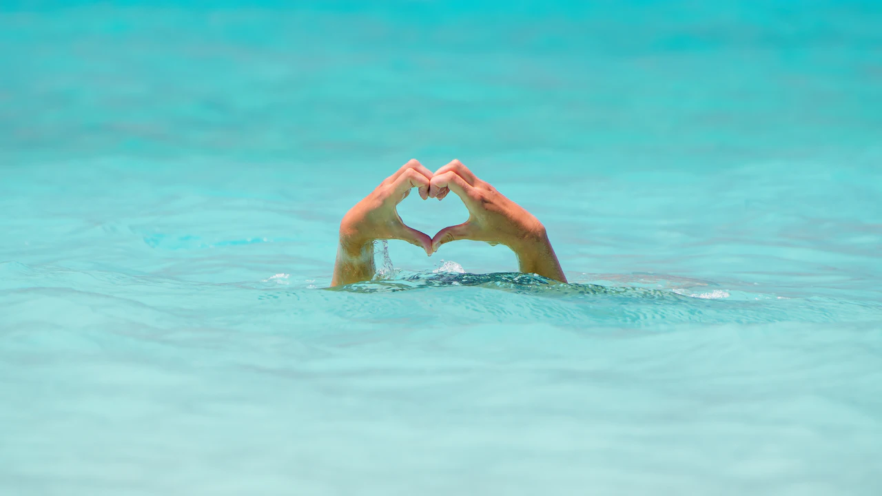 Swimmer making a heart shape with both hands in clear water