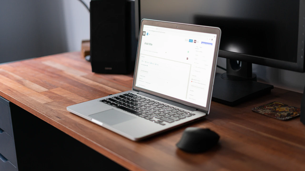 Open laptop on a wooden desk beside a monitor and speaker