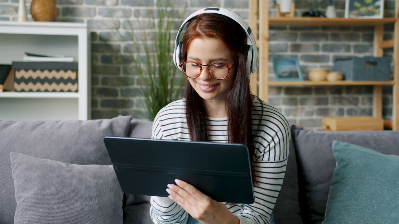 Woman in headphones studying on a tablet while sitting on a sofa