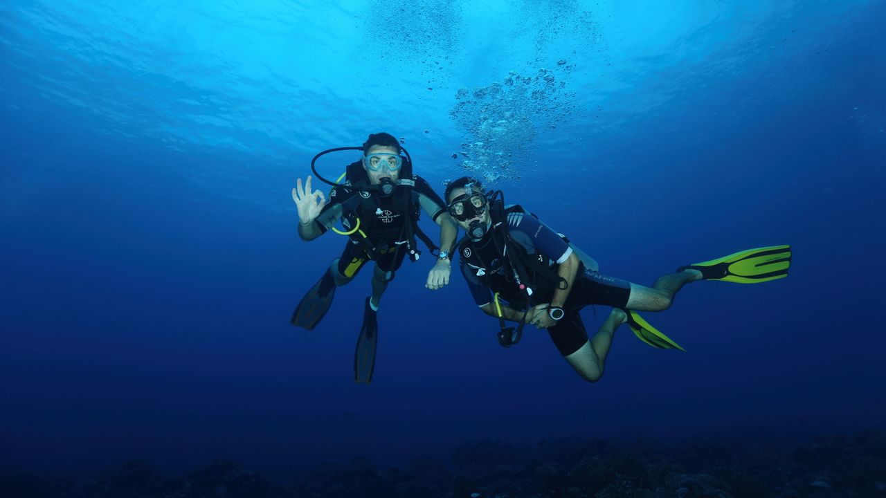 Two divers swimming side by side and staying close as buddies