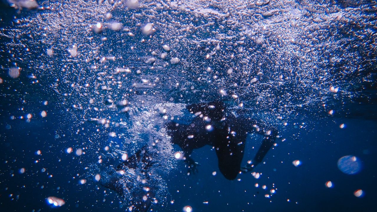 Relaxed diver hovering motionless as a stream of bubbles rises overhead