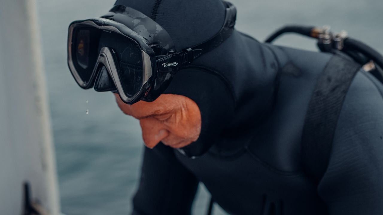 Diver in a hooded wetsuit and mask on a boat
