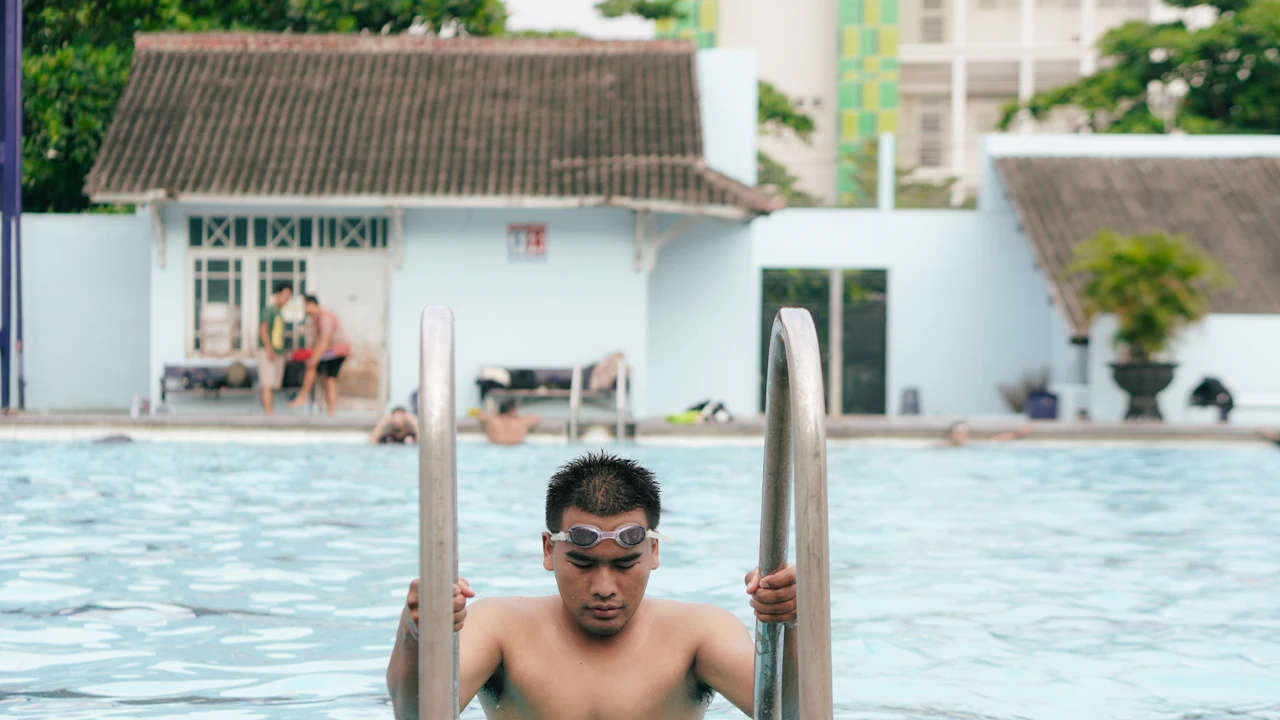 Man climbing out of an outdoor swimming pool by the ladder