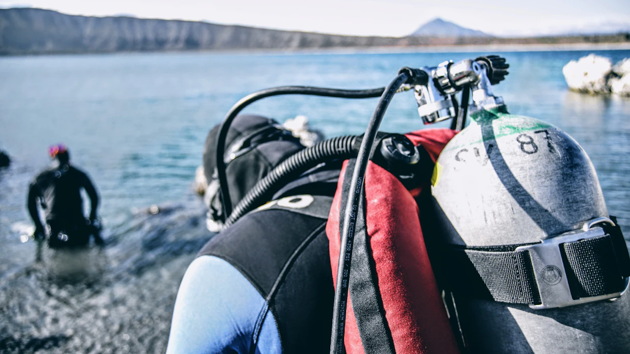 Divers in wetsuits with tanks getting ready on a rocky shore