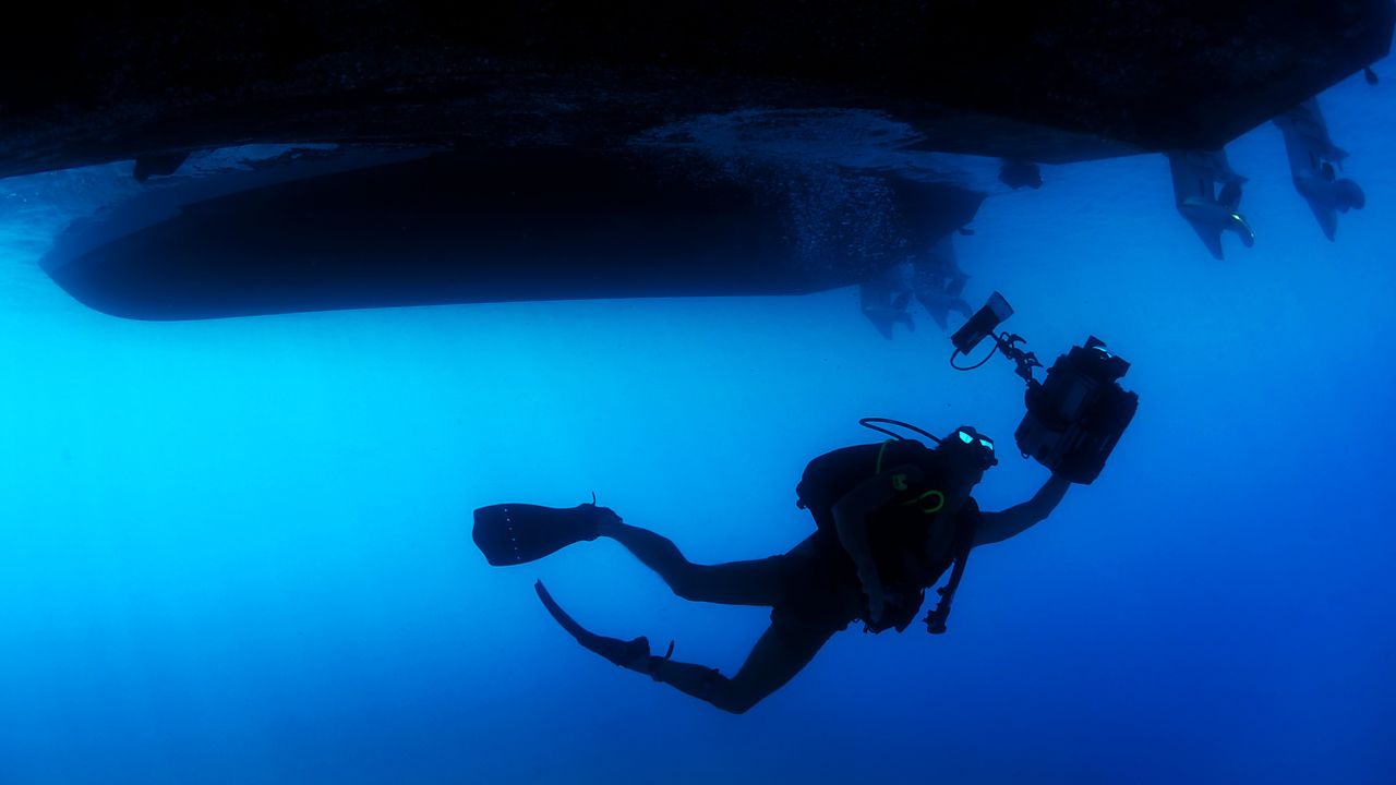 Diver silhouetted below a boat hull