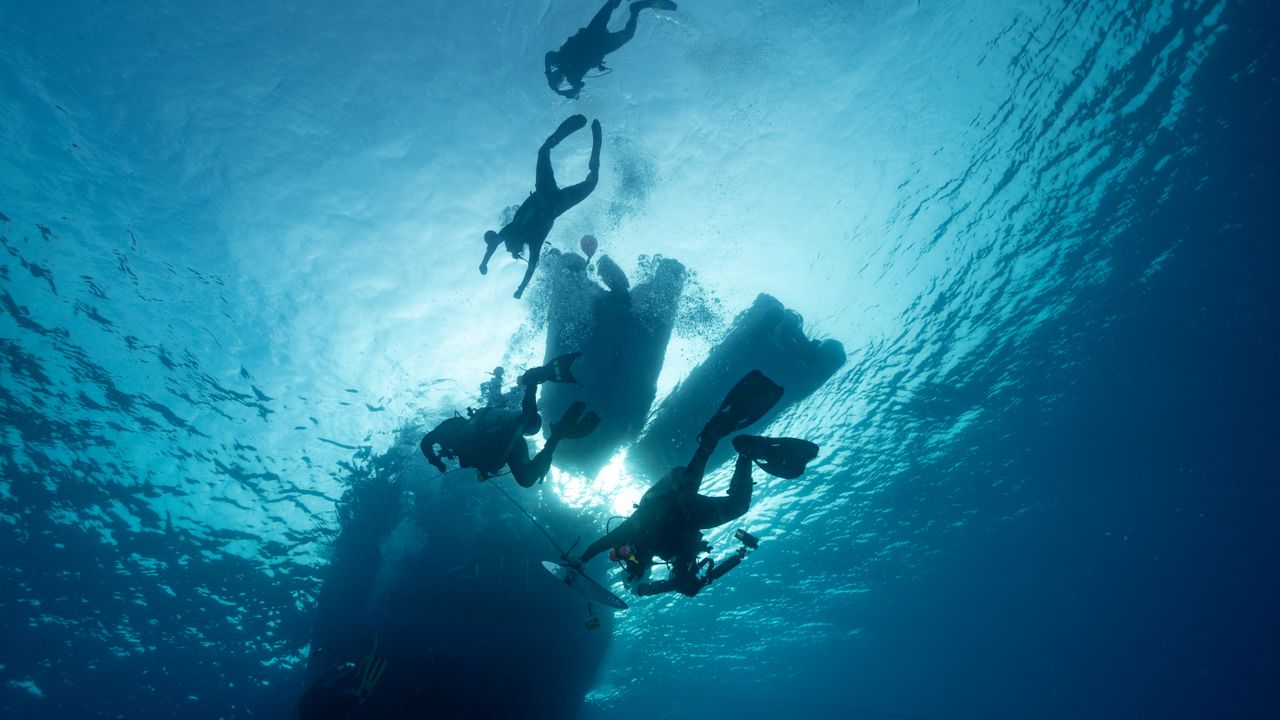 Two scuba divers ascending slowly toward a bright water surface