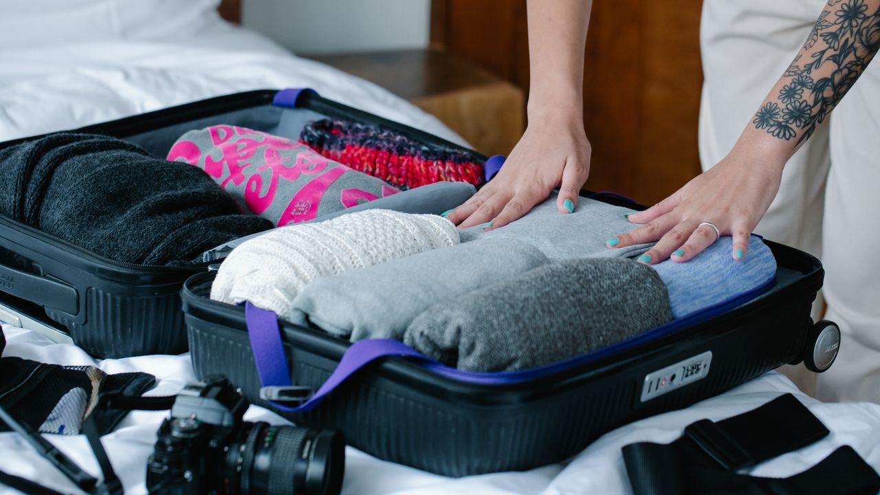Traveler packing clothes into a suitcase on a bed