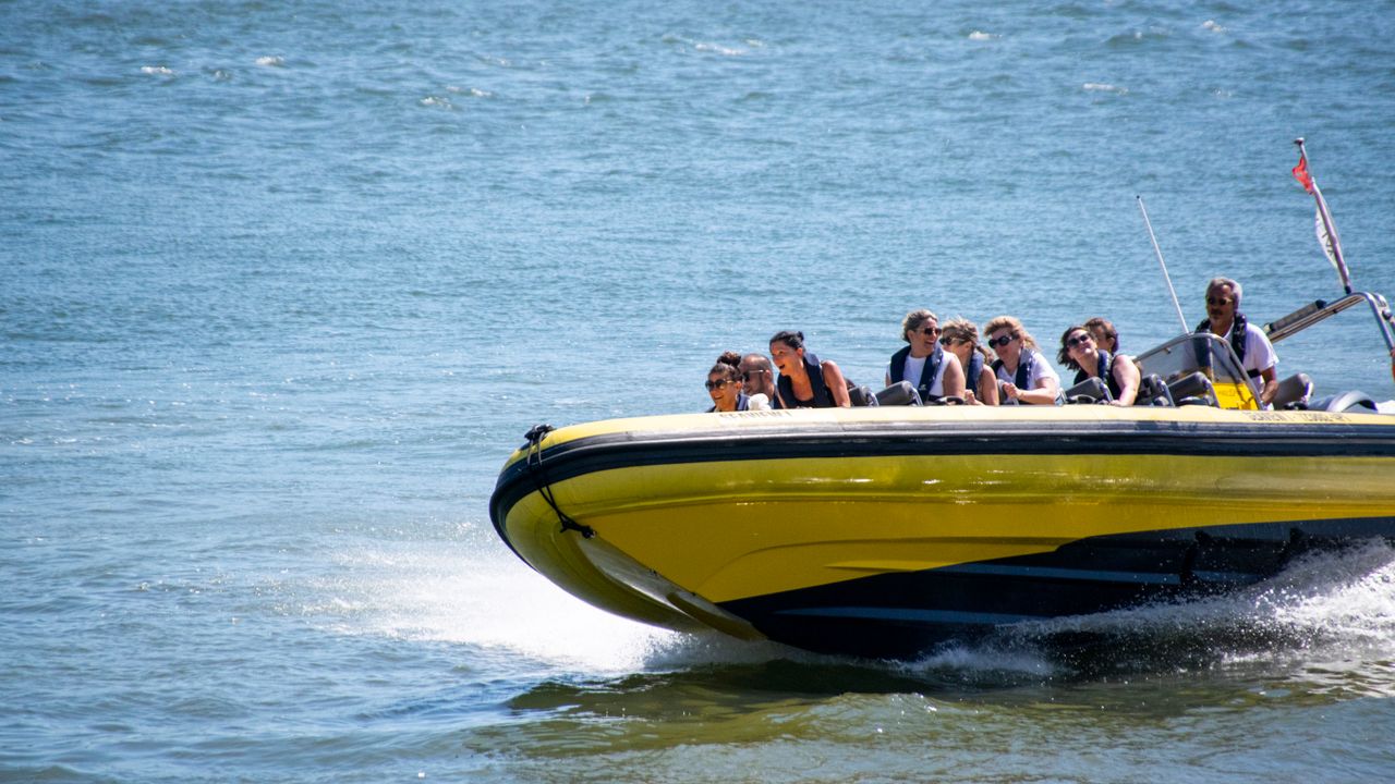 Passenger speedboat crossing calm blue water with a white wake behind it