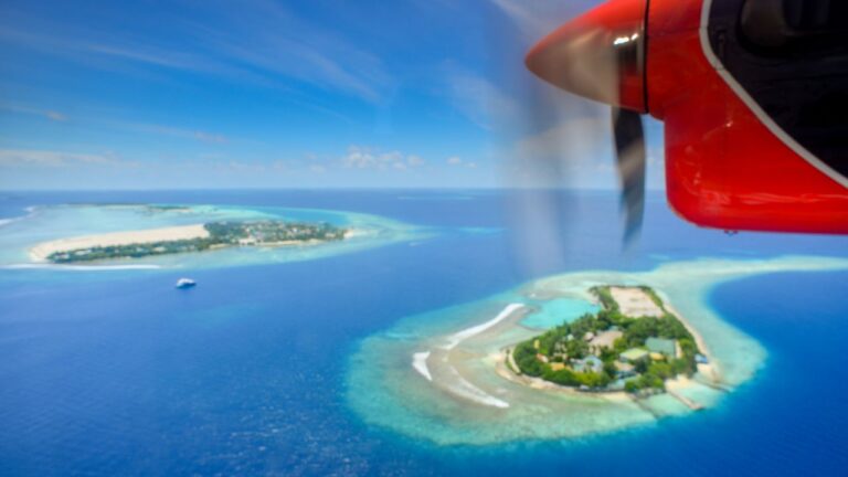 Small propeller plane flying low over turquoise sea and scattered green islands
