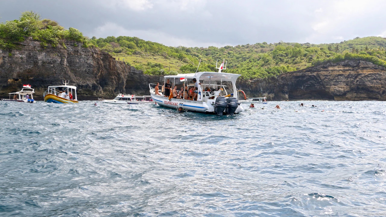 Tour boats anchored below green cliffs with snorkelers nearby