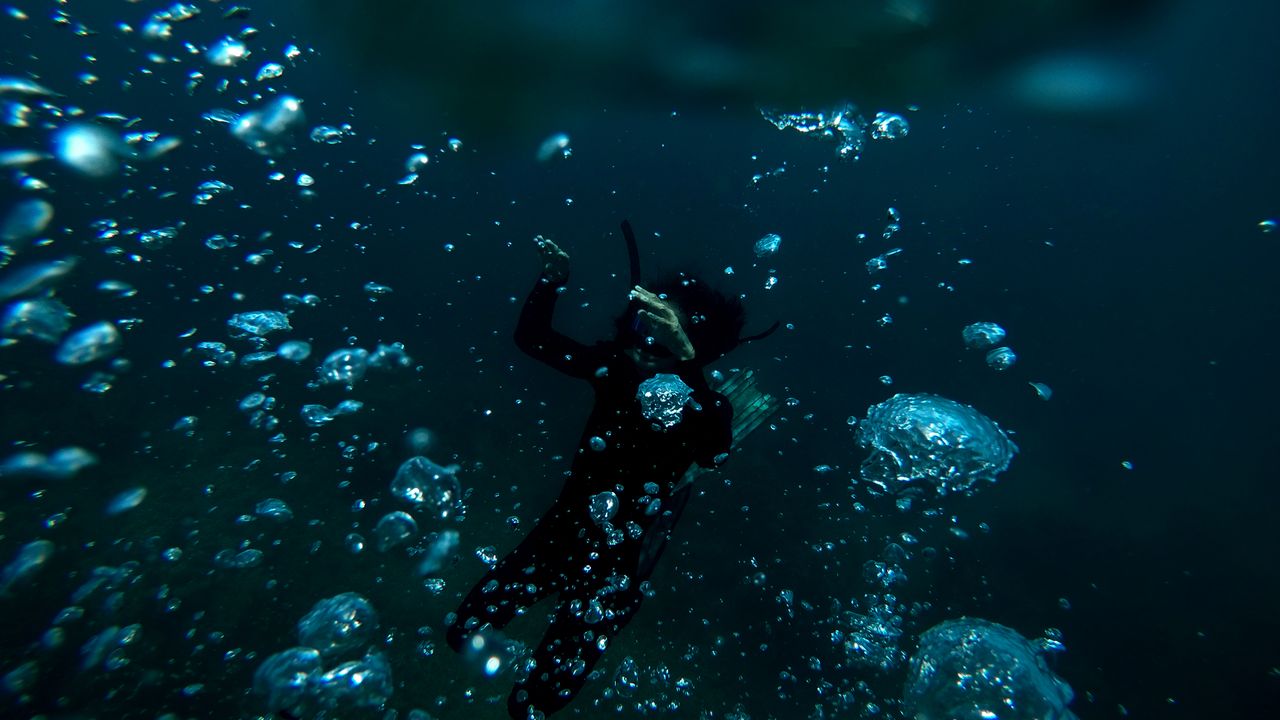 Scuba diver surrounded by rising bubbles in dark blue water