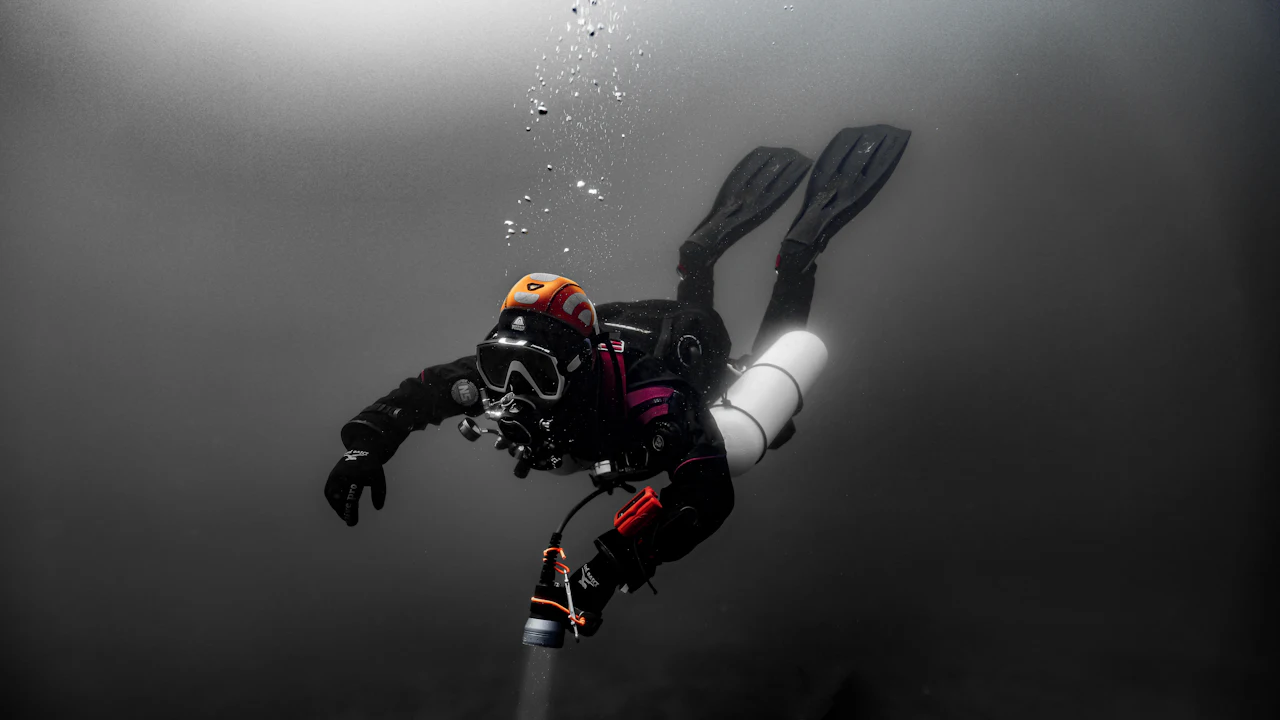 Scuba diver wearing a dark mask and helmet swimming in open water