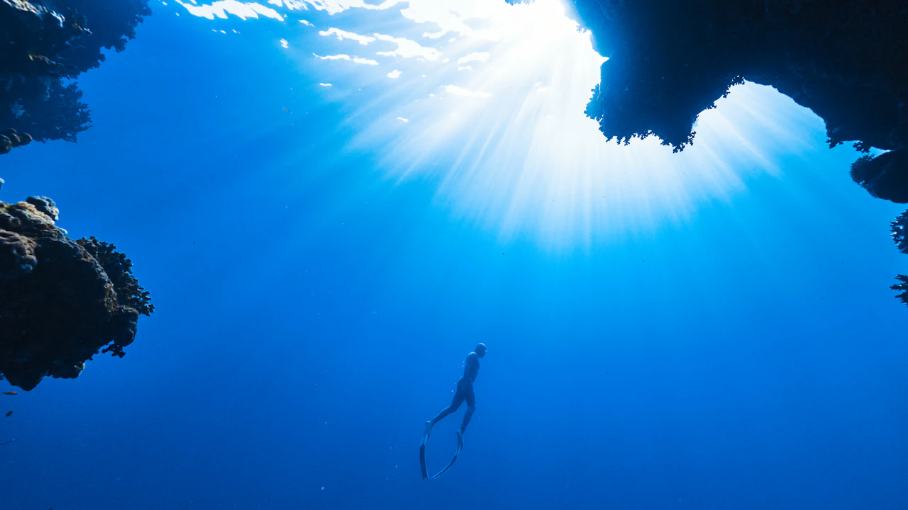 Free diver swimming down below a sunlit opening in the rock