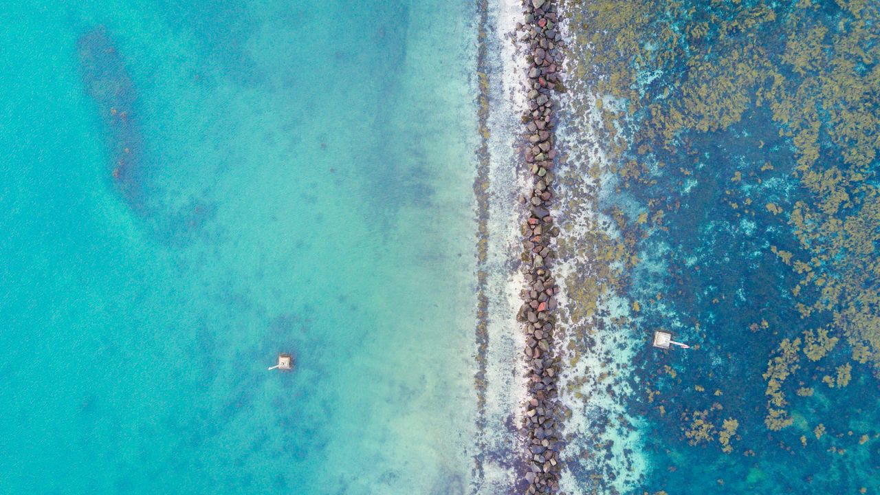 Aerial view of turquoise shallows split by a long rocky reef line