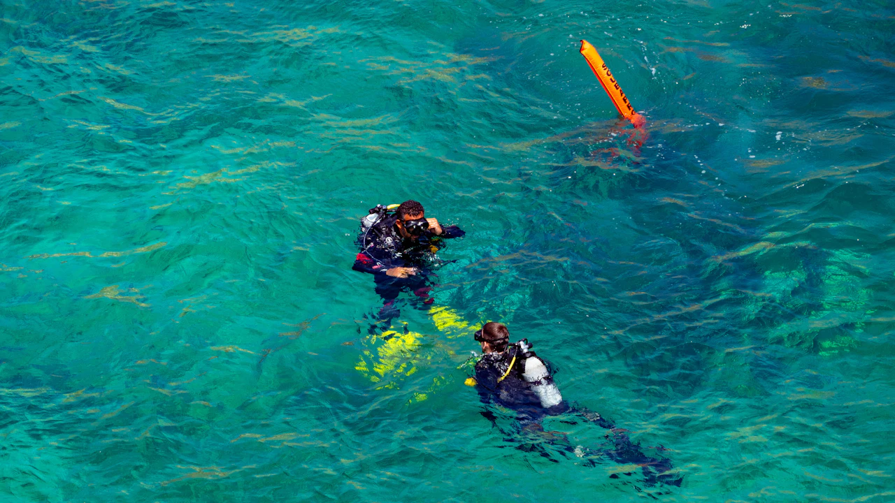 Two scuba divers near the surface beside an orange marker buoy