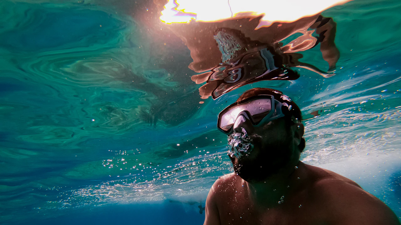 Man in a mask exhaling bubbles through his nose just below the surface