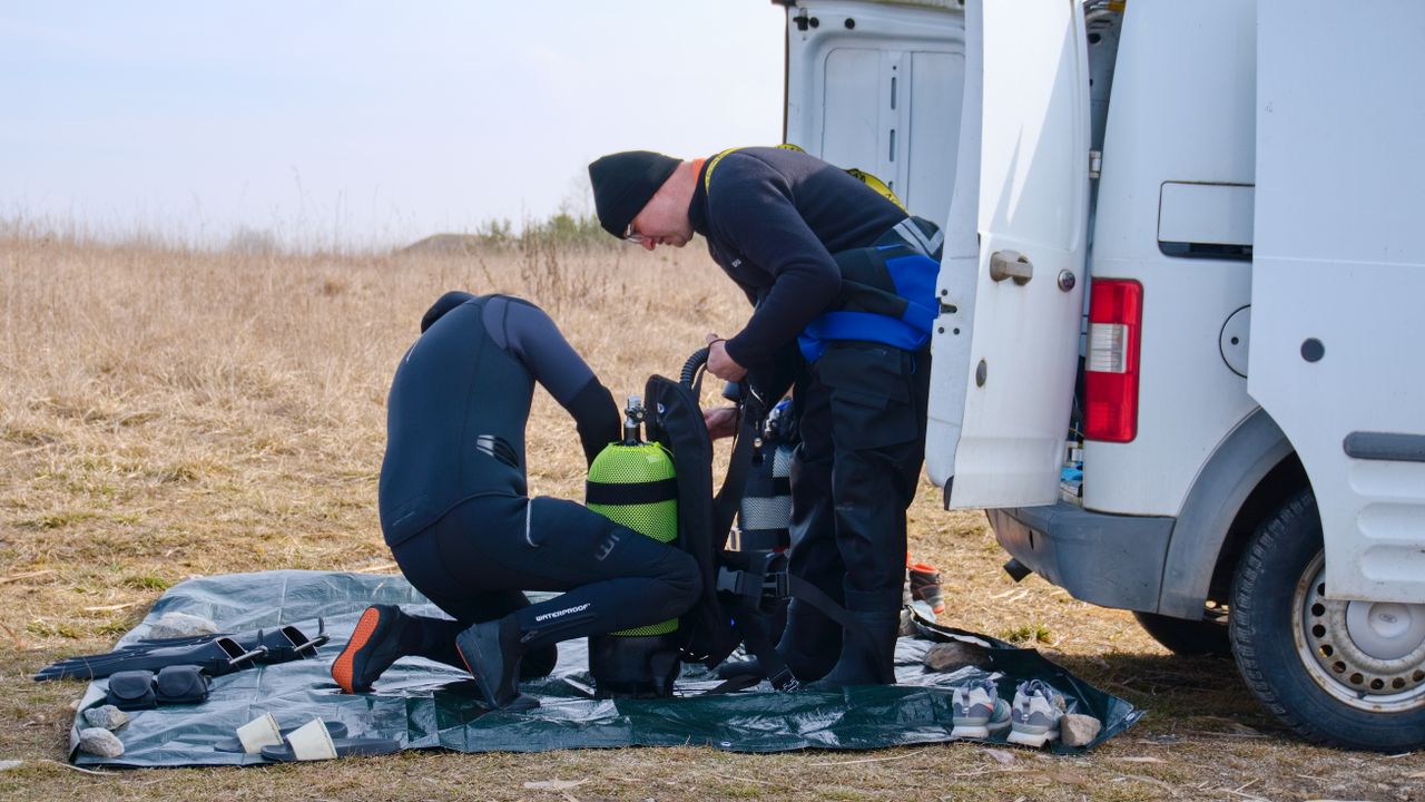 Two divers putting on gear beside a van